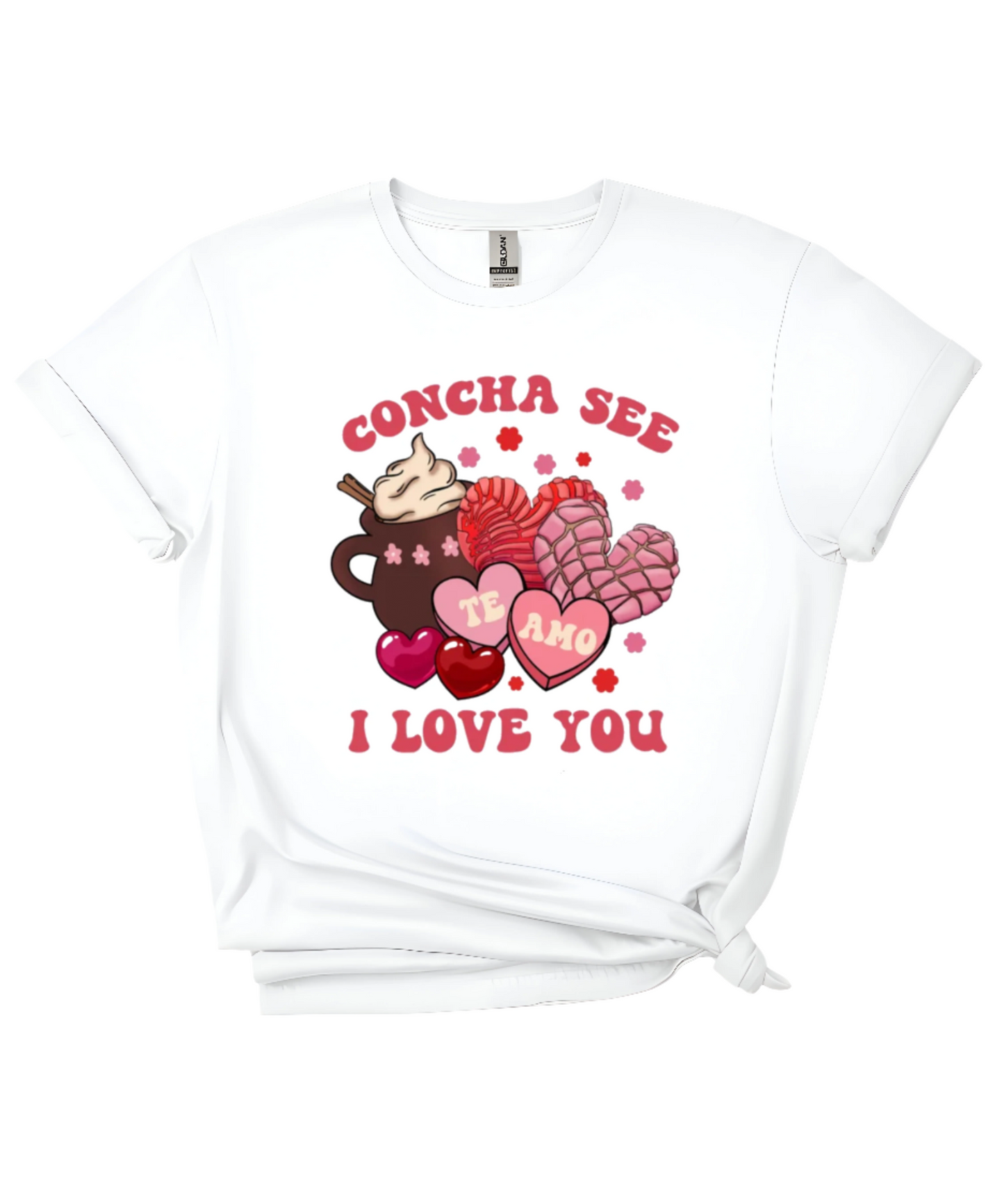 A white t-shirt featuring a festive Valentine’s Day-inspired design with the phrase “CONCHA SEE I LOVE YOU” in bold red letters. The graphic includes a cup of hot chocolate topped with whipped cream, two pink and red conchas (Mexican sweet bread), and heart-shaped candies with “TE AMO” written inside. Small flowers and hearts surround the design, adding a cute and romantic touch. Perfect for cozy, food-themed apparel lovers.