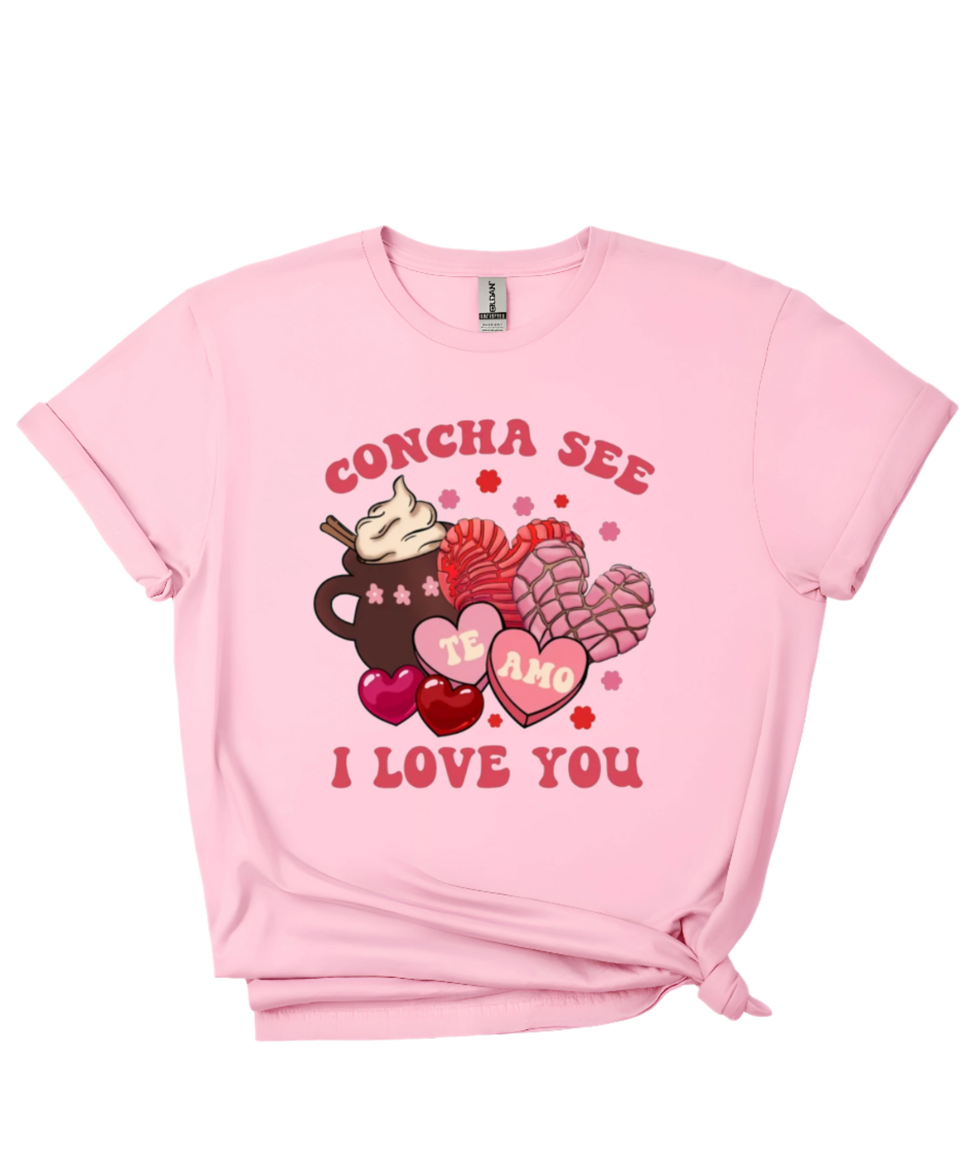 A pink t-shirt featuring a festive Valentine’s Day-inspired design with the phrase “CONCHA SEE I LOVE YOU” in bold red letters. The graphic includes a cup of hot chocolate topped with whipped cream, two pink and red conchas (Mexican sweet bread), and heart-shaped candies with “TE AMO” written inside. Small flowers and hearts surround the design, adding a cute and romantic touch. Perfect for cozy, food-themed apparel lovers.