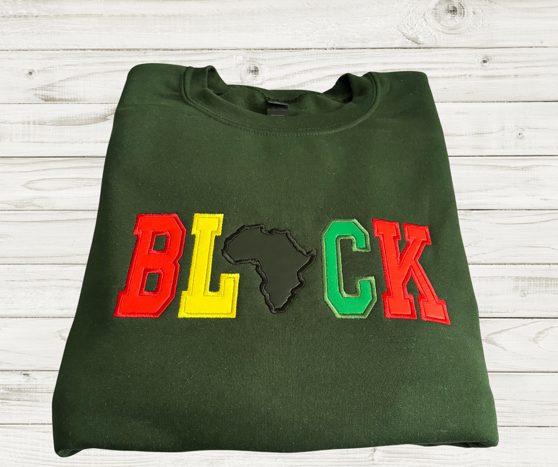 Dark green crewneck sweatshirt featuring bold, varsity-style appliqué lettering that spells out “BLACK.” The letters are in red, yellow, and green, with the letter “A” replaced by a black embroidered shaped of the African continent.